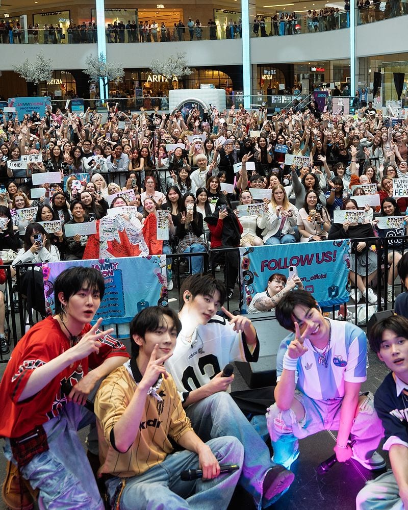 A K-pop group posing with JAMMY CON fans after a live performance.